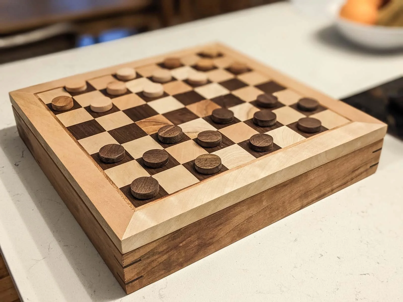 A wooden chess and checkers board on a white surface, with checkers pieces set up.