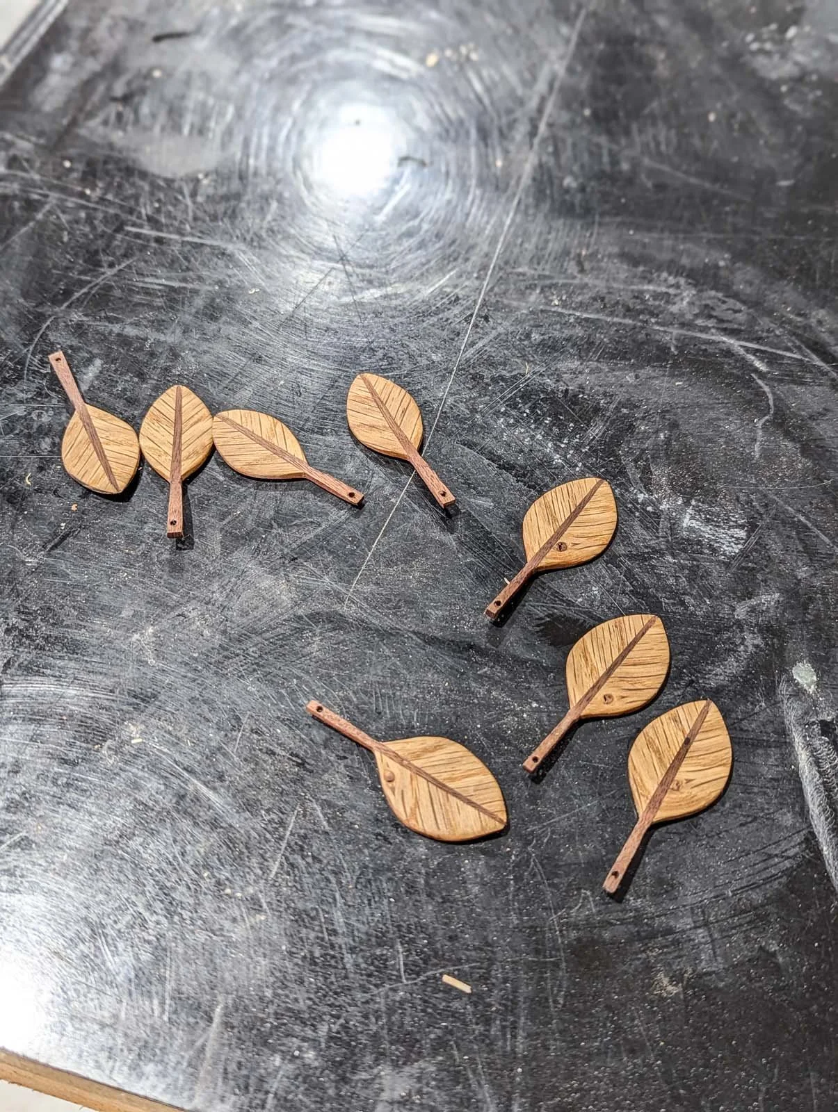 Several small wooden leaf-shaped pieces arranged on a dark, scratched work surface.