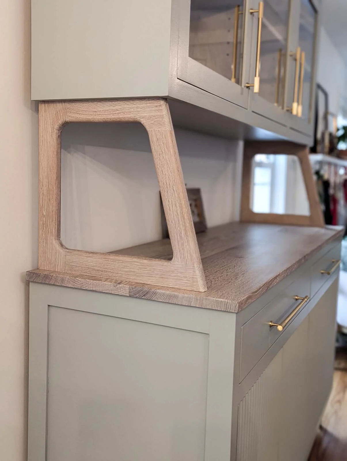 Close-up of a modern kitchen sideboard with light grey cabinetry, gold handles, and wooden open shelves with angled supports.