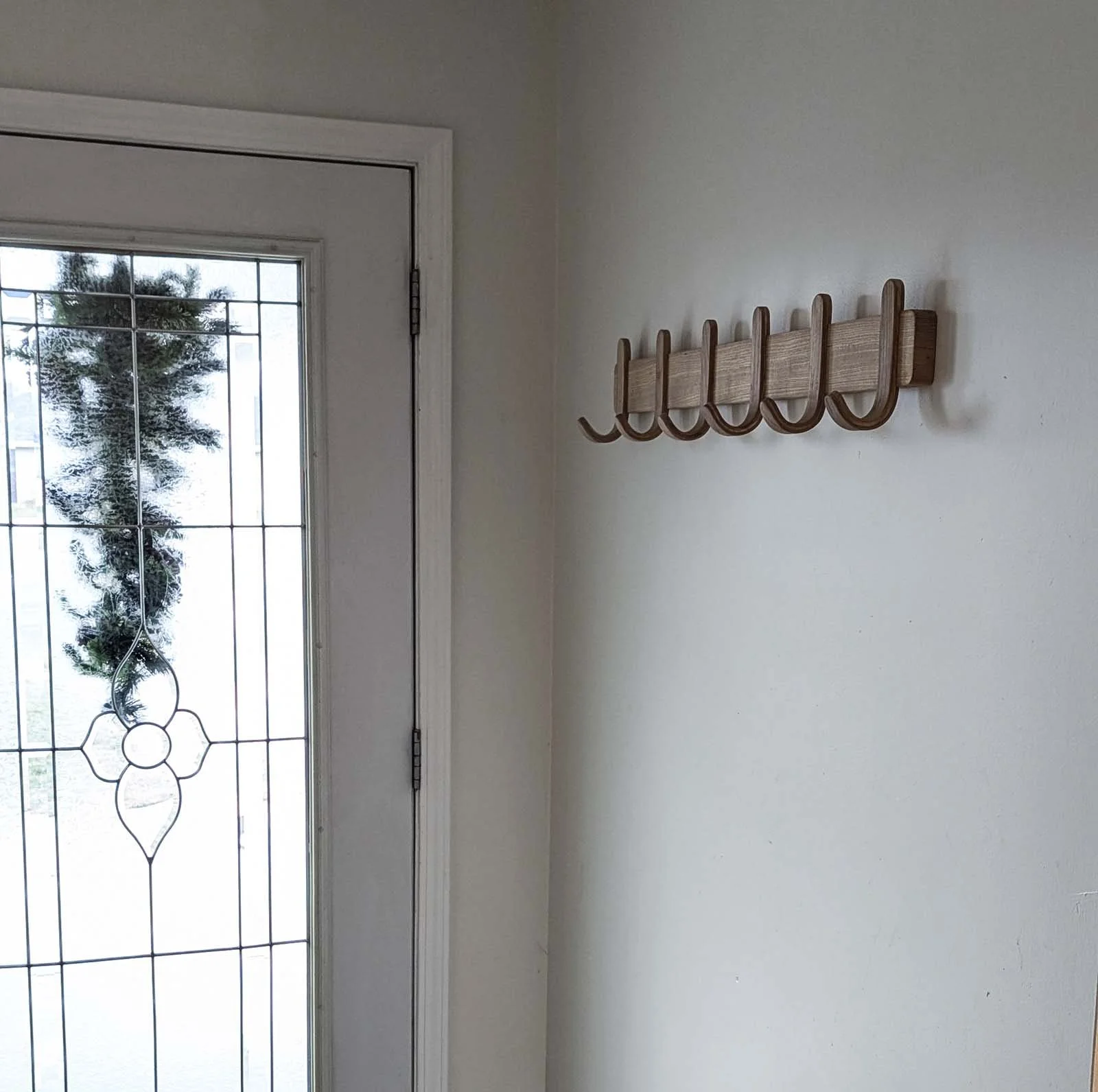 A wall with a wooden coat rack and a door with glass panel and decorative metal grille.