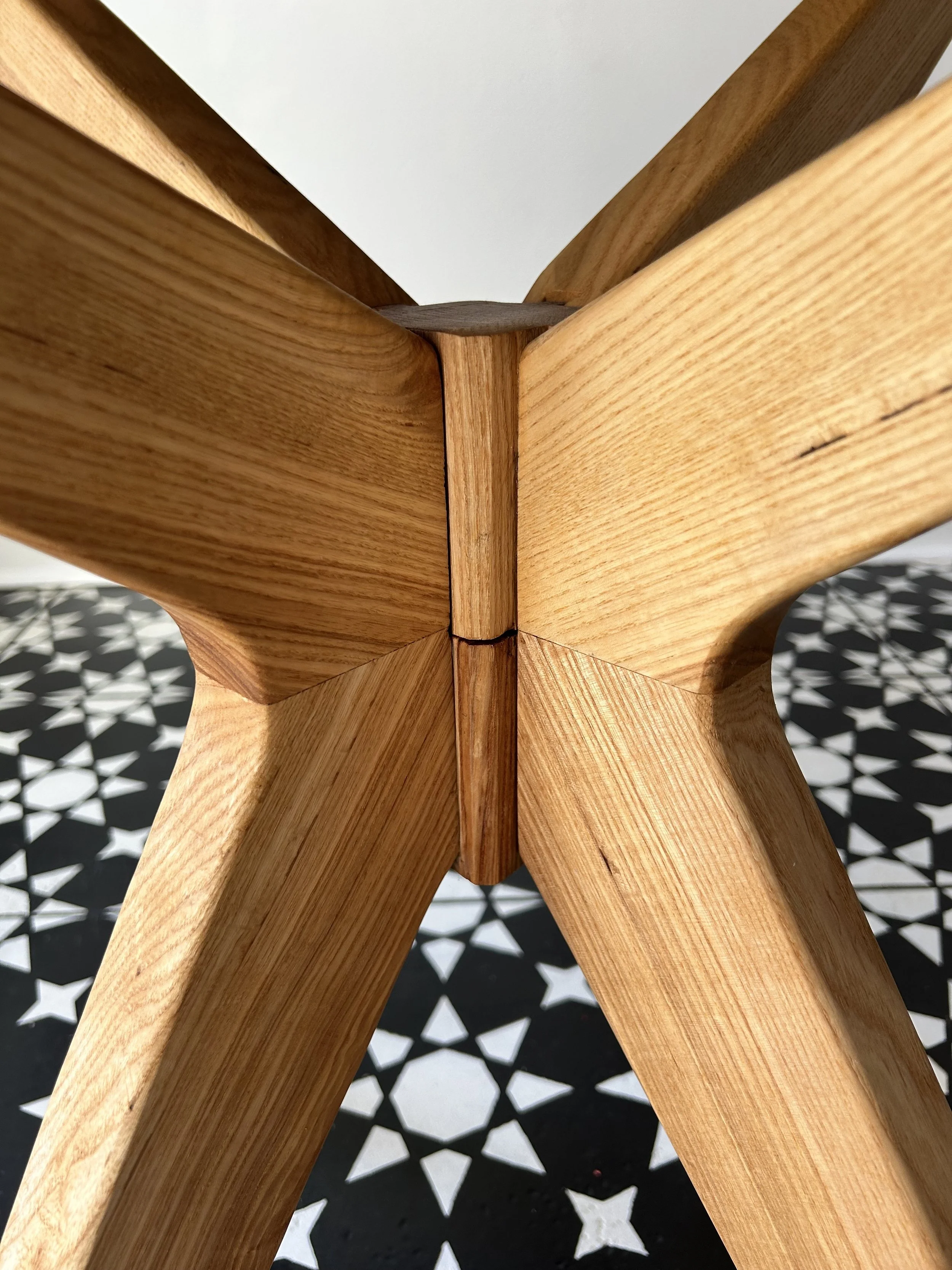 Close-up view of the joint of a wooden chair or table showing the intersecting wood grain with a geometric patterned black and white floor in the background.