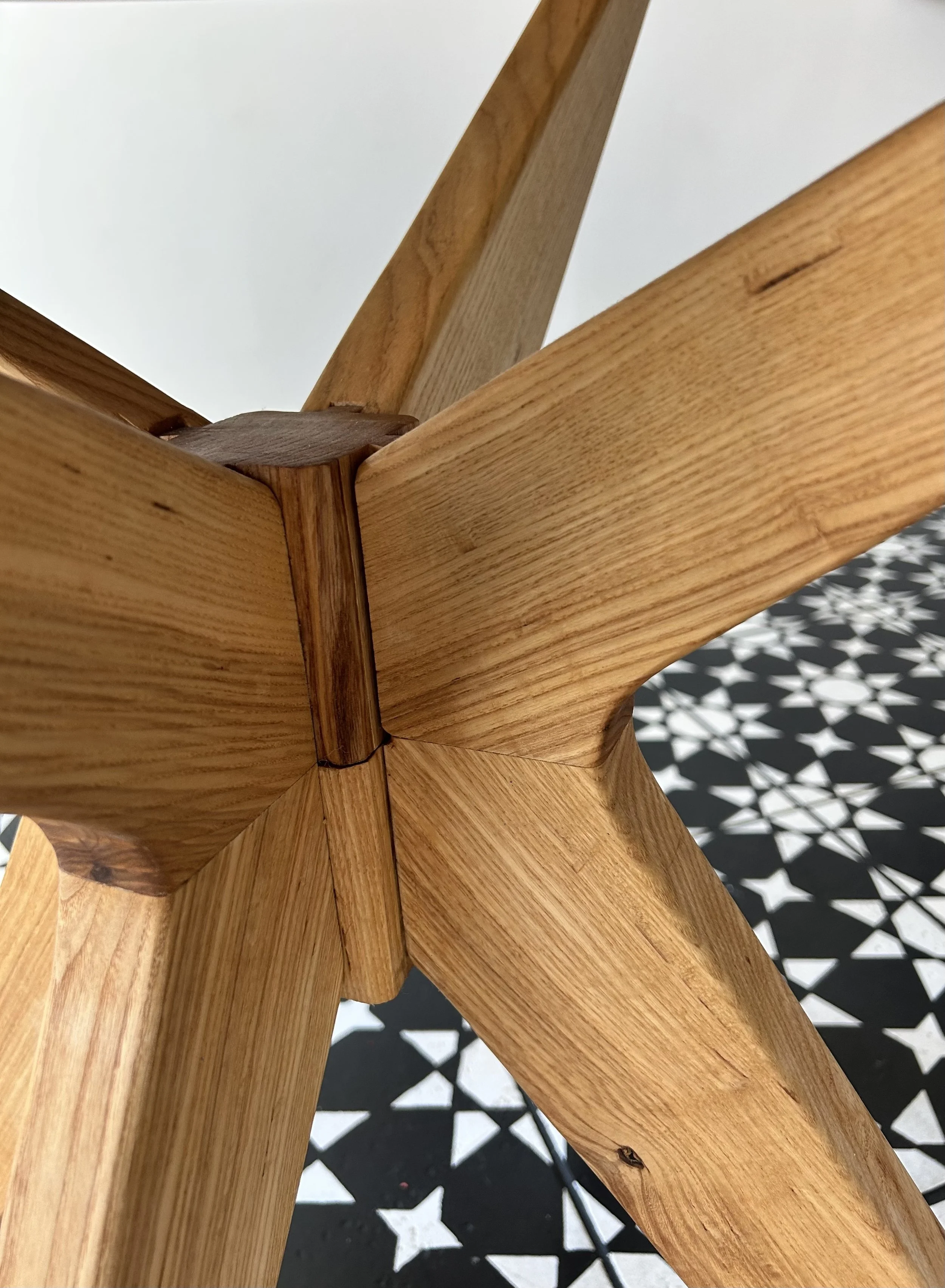 Close-up of a wooden furniture joint where four pieces of wood are connected, with a patterned black and white floor in the background.