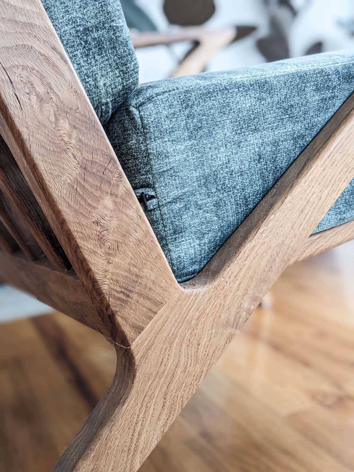 Close-up of a wooden chair armrest next to a blue upholstered seat with textured fabric.