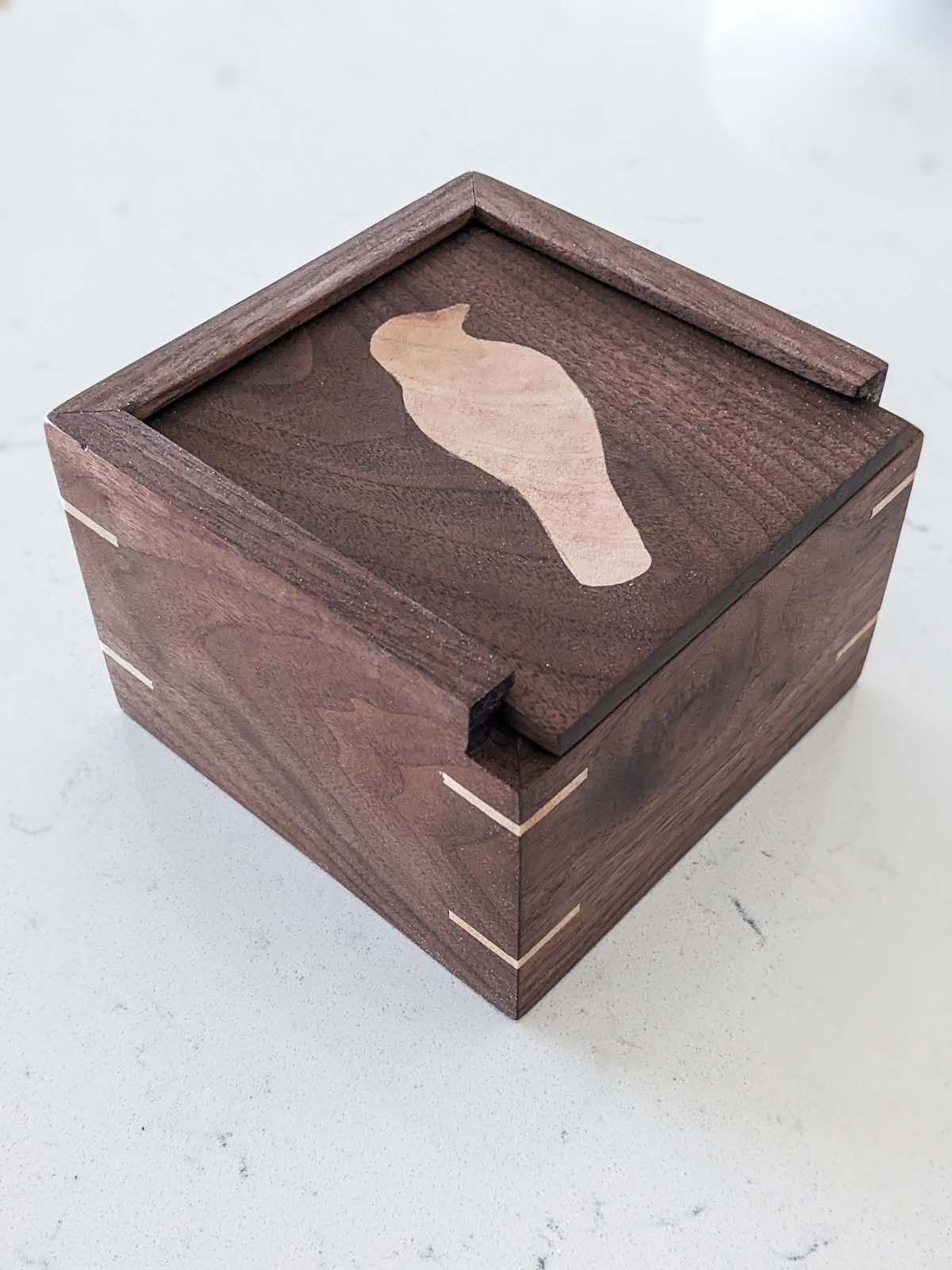 A small wooden box with dovetail joints and a inlay of a bird silhouette on the top surface.