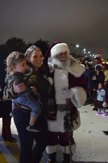 A young family taking advantage of a photo opportunity with Santa Claus at an outdoor event at night.