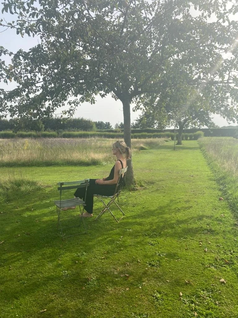 Emma Holland of Emma Holland Gardens, sitting in a beautiful naturalistic orchard garden in France
