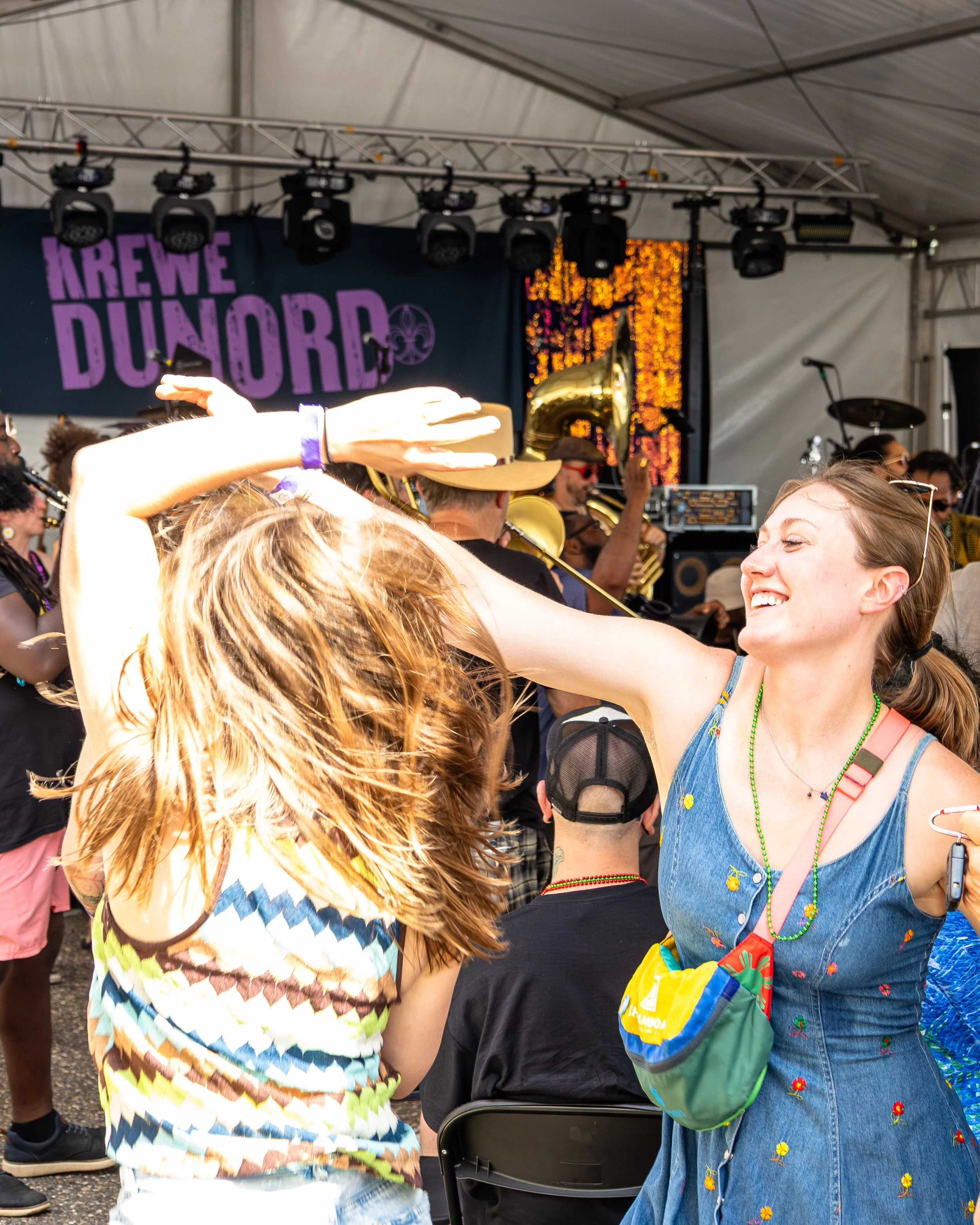 Two women dancing and enjoying music at an outdoor concert with a band playing on stage in the background.