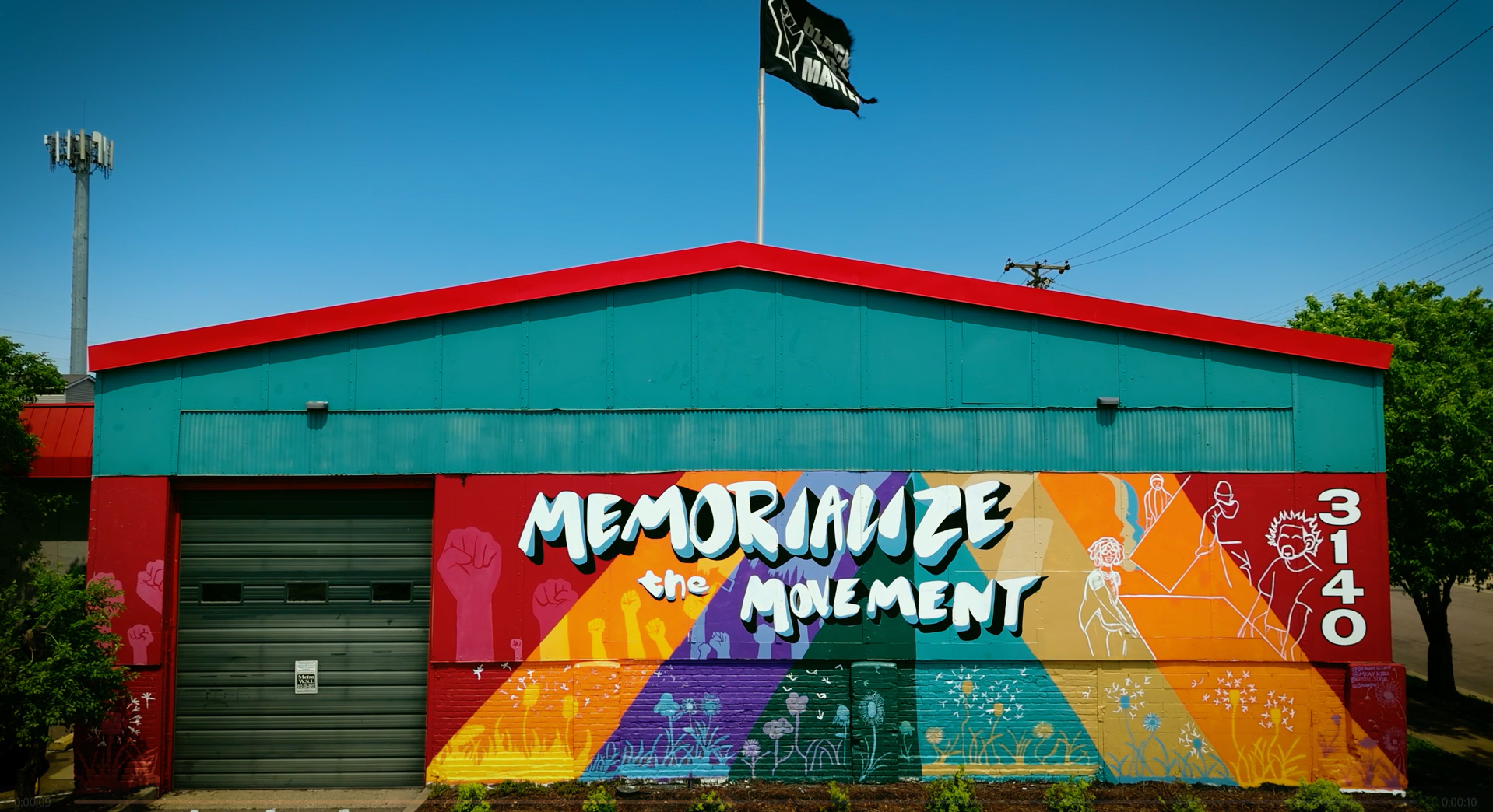 Building with a colorful mural that reads "Memorialize the Movement" and features illustrations of people protesting with raised fist symbols and nature imagery.