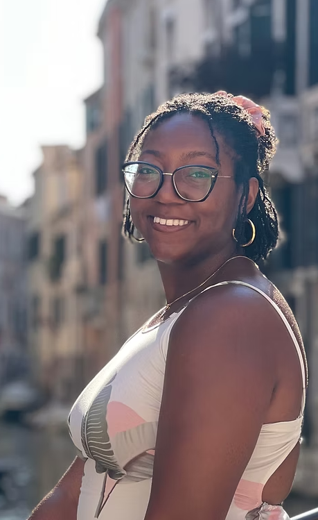 Smiling woman with glasses and hoop earrings standing outdoors in a city street with blurred buildings in the background.