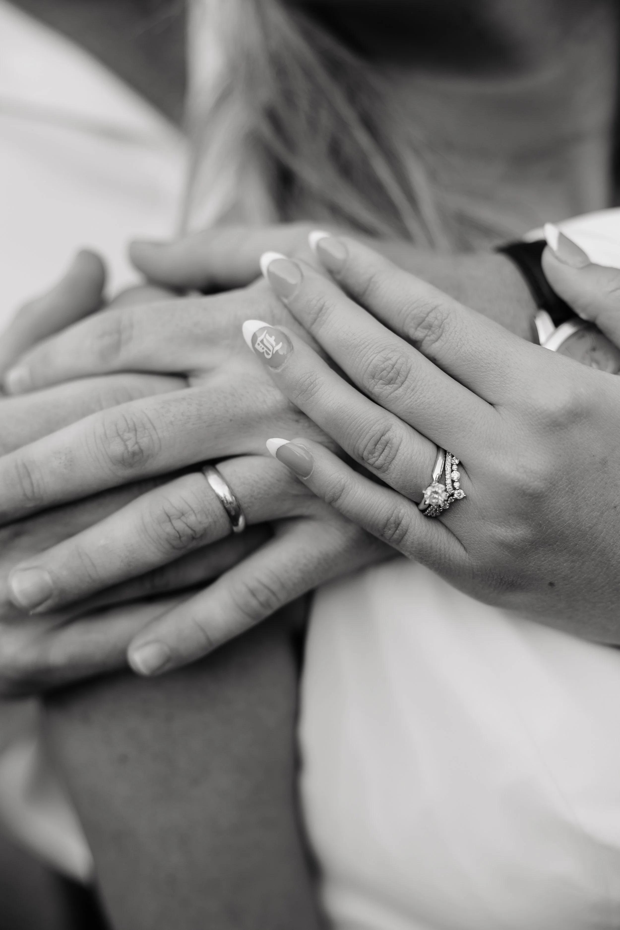 Close-up of multiple hands layered on top of each other, showing wedding and engagement rings.