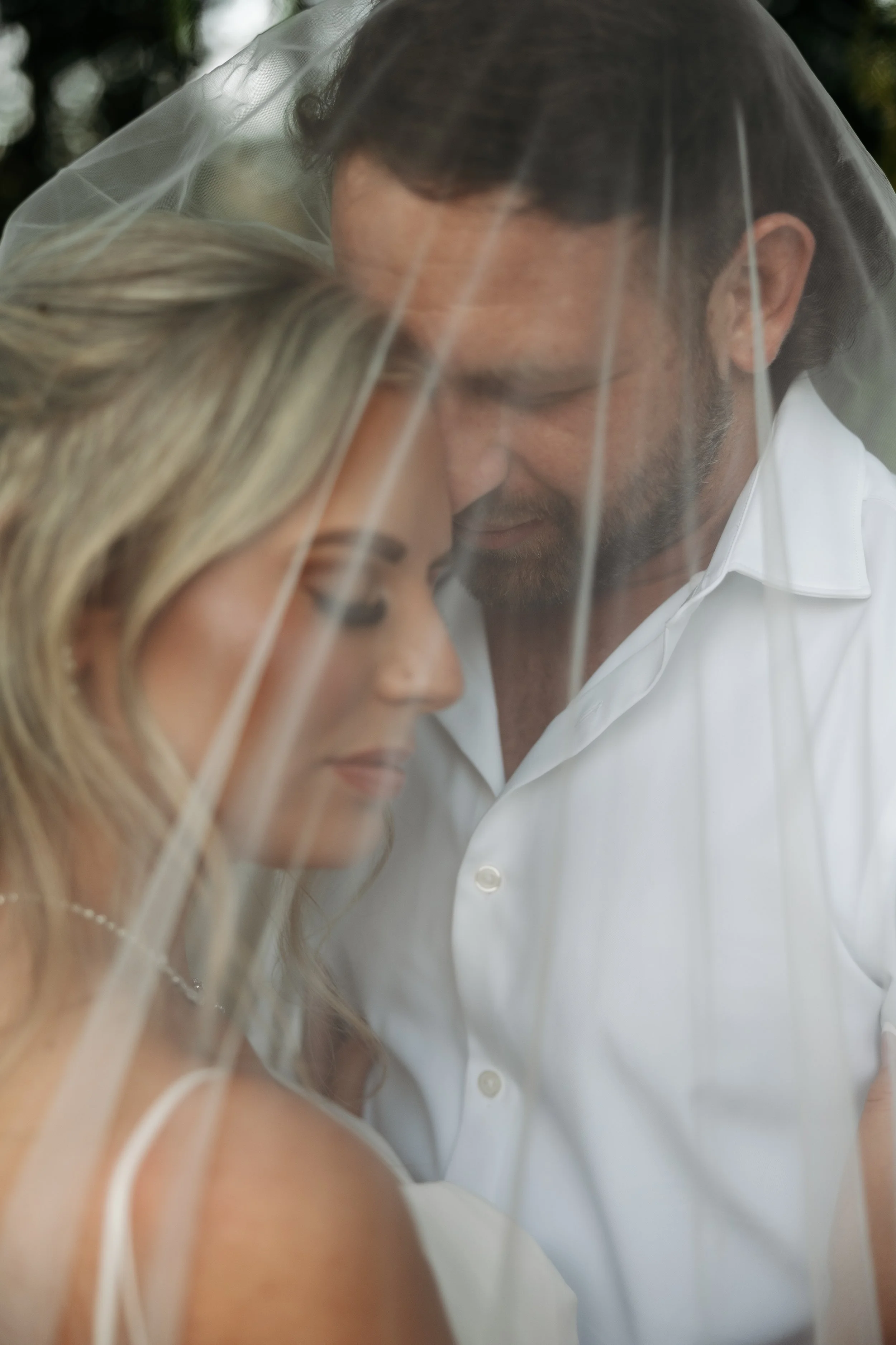 Close-up of a bride and groom sharing a tender moment with their foreheads touching under a bridal veil.