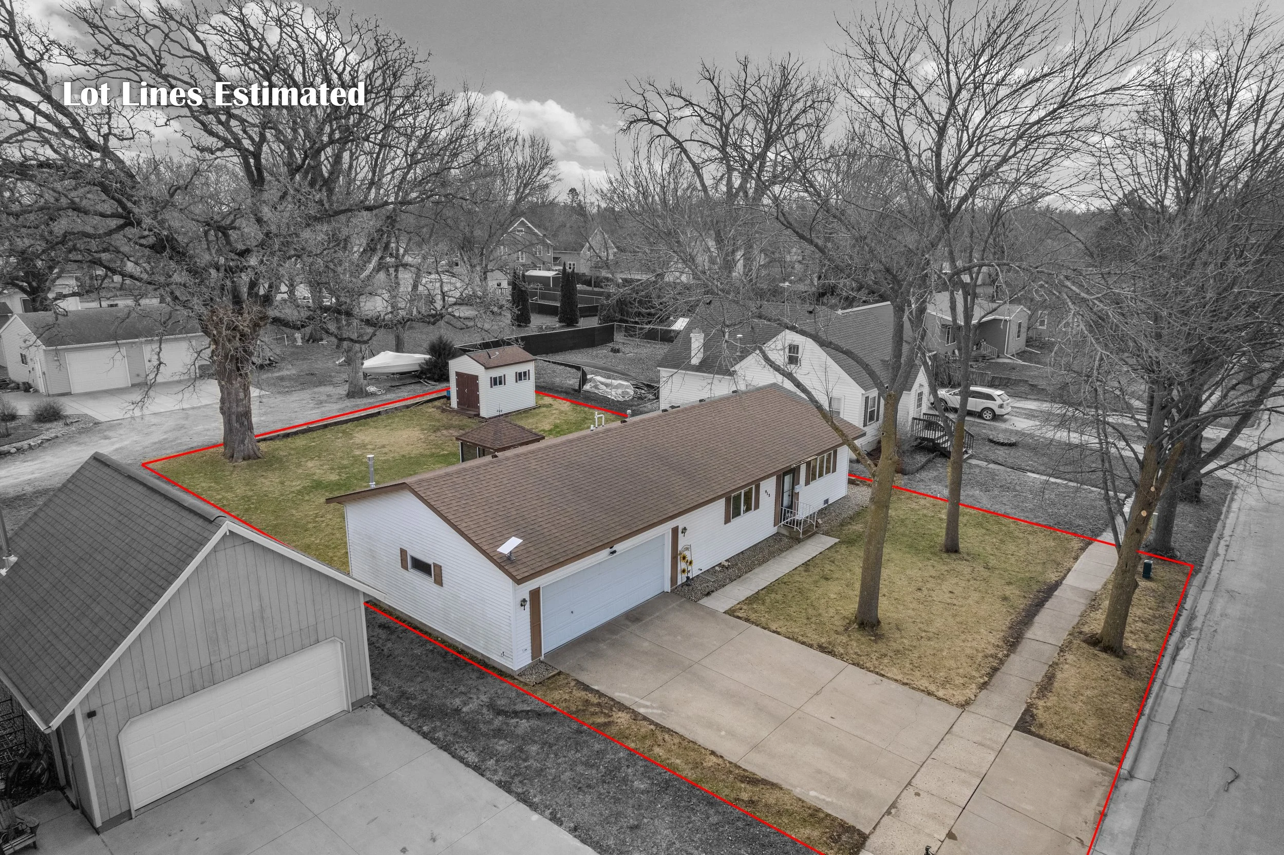 A backyard with a house, a small shed, a lawn, trees, and a cloudy sky in the background. The edge of the yard is marked with a red line estimate for lot lines.