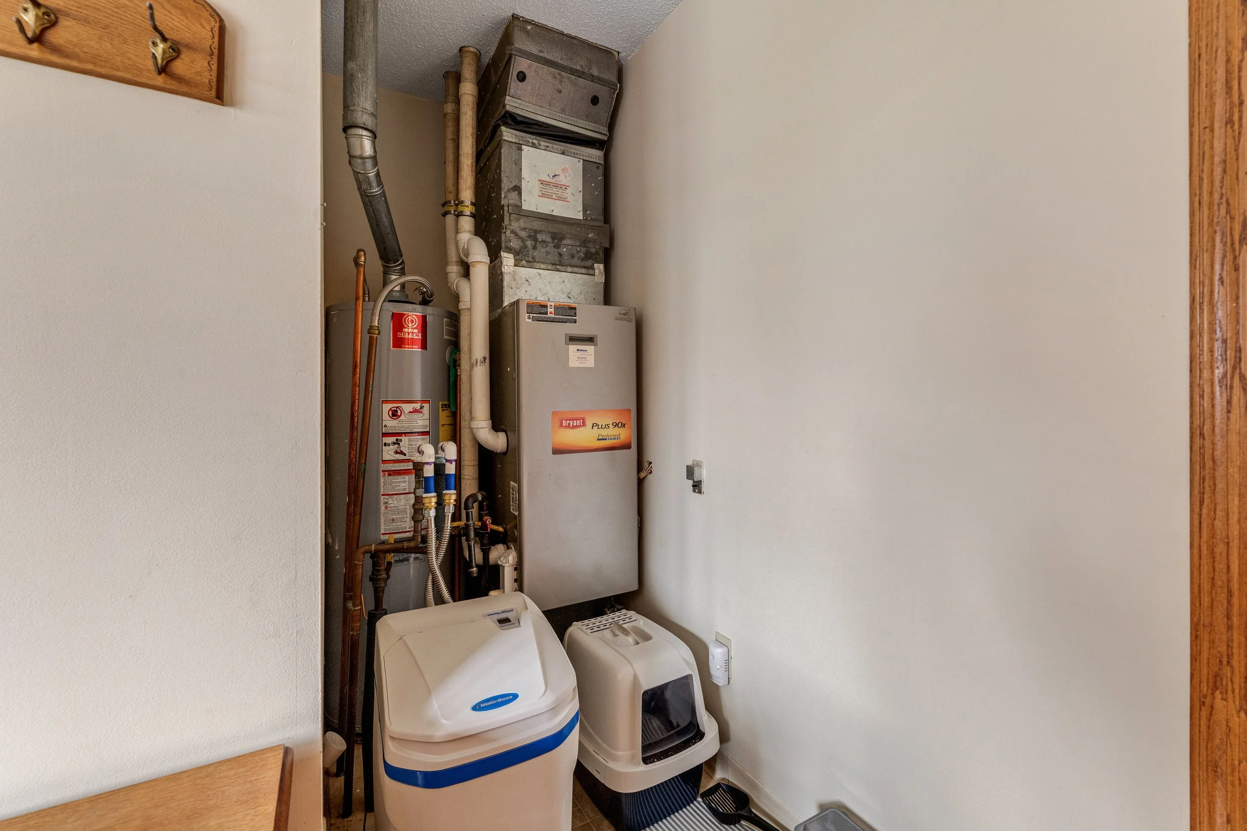A small laundry room with a utility sink, energy furnace, and hot water heater, with hooks on the wall and a chair visible in the foreground.