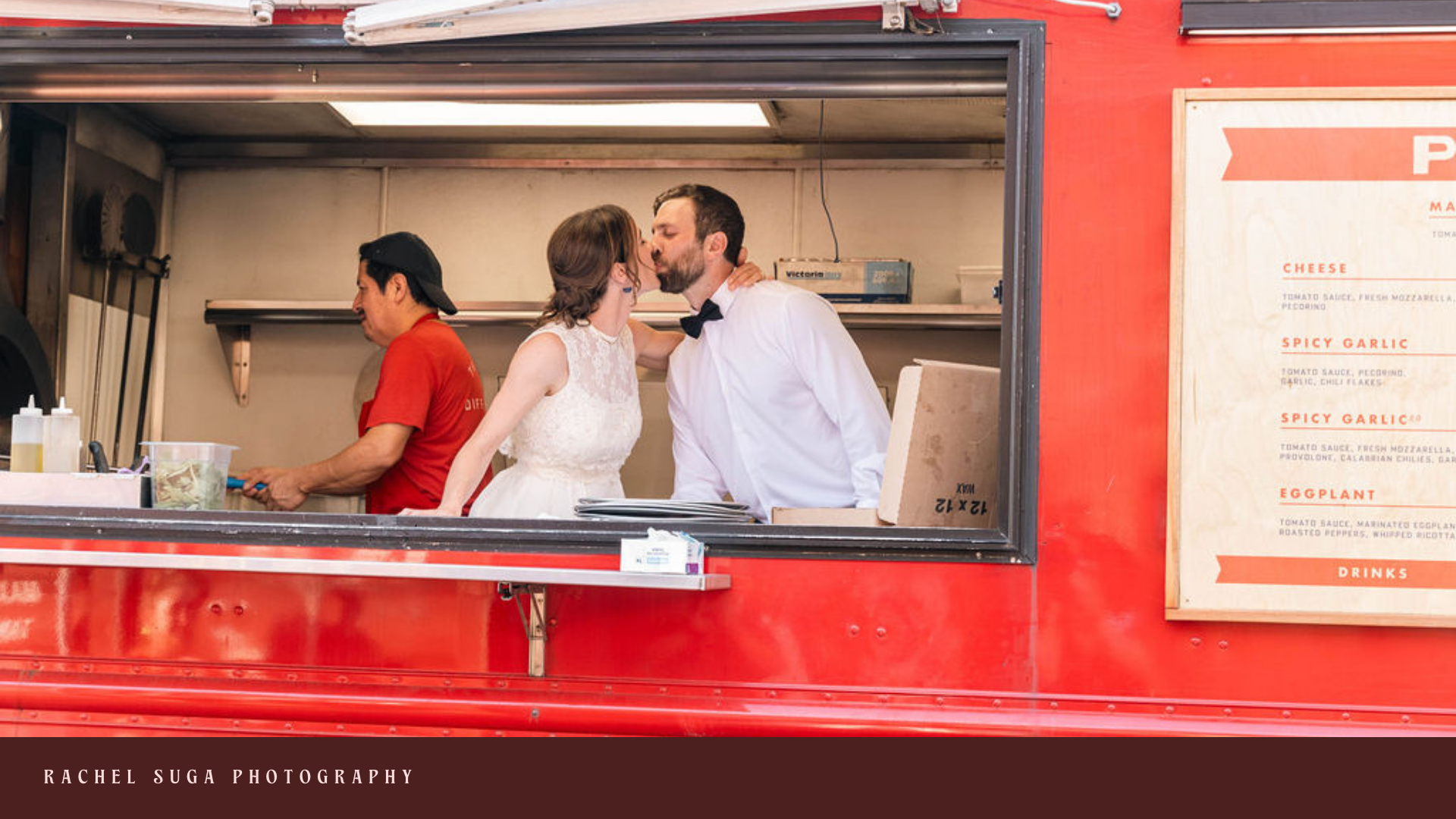 A couple dressed in wedding attire sharing a kiss inside a food truck, with a man in a red shirt preparing food in the background.