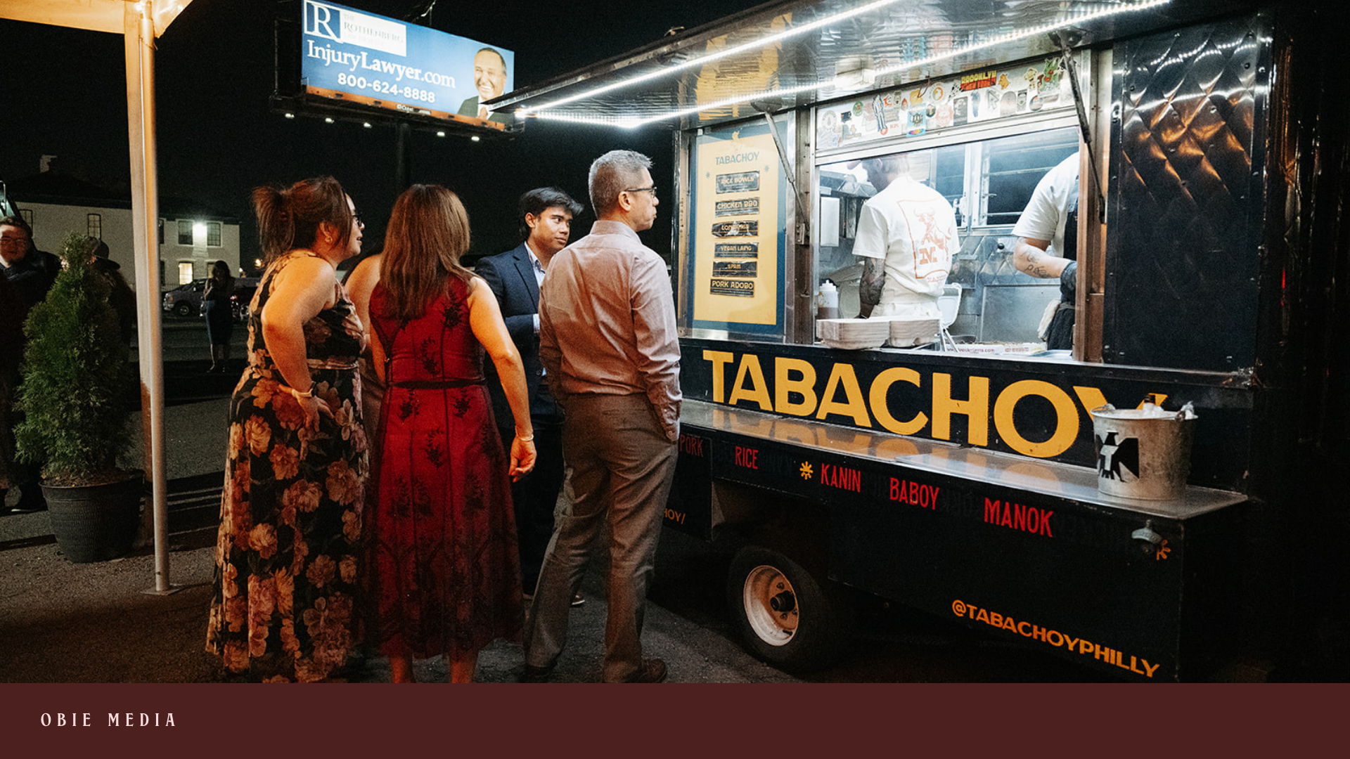 People standing in line at a nighttime food truck called Tabachoy, which offers dishes like pork, rice, chicken adobo, and others, with the operators preparing food inside.