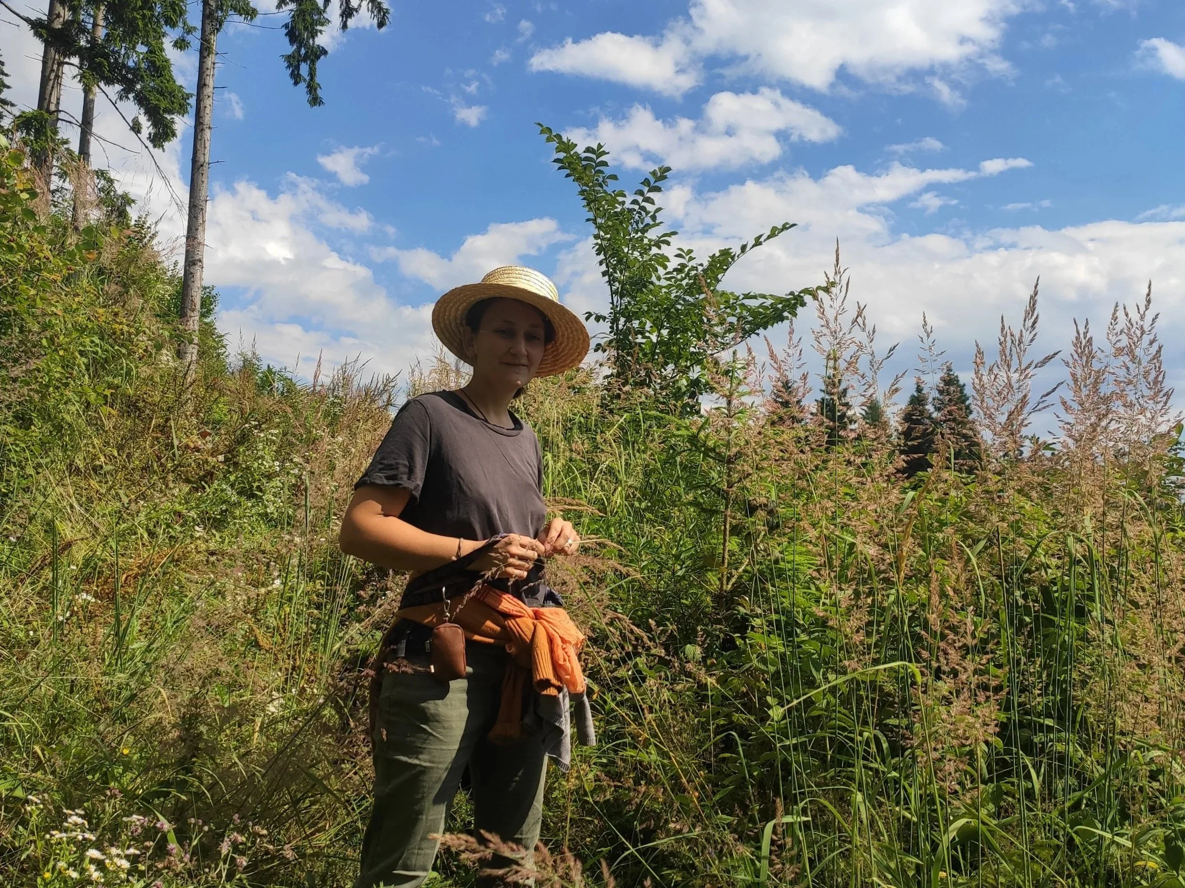 Eine Frau mit Hut steht in hoher Vegetation.