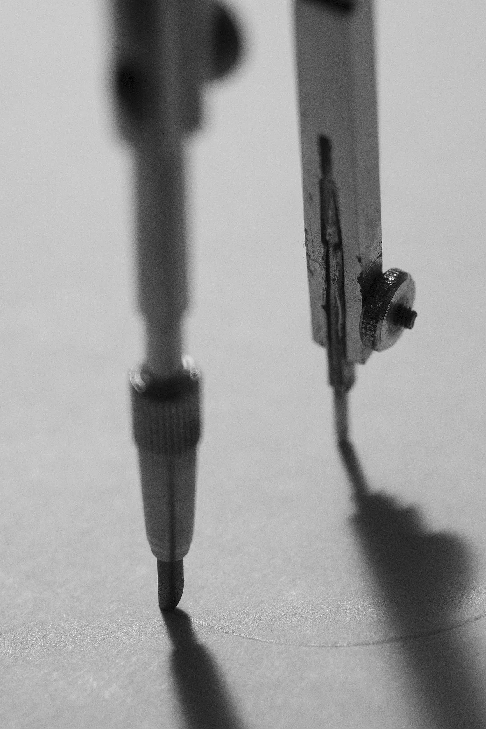 Close-up of a metal drafting compass on a light surface, with the needle and one arm visible in black and white.