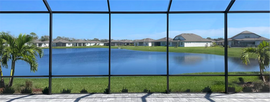 View of a residential lake from inside a screened porch with palm trees and grass