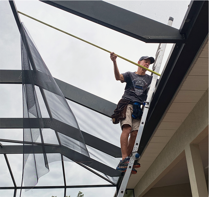 Man standing on a ladder, cleaning or repairing the roof of a house on a cloudy day.