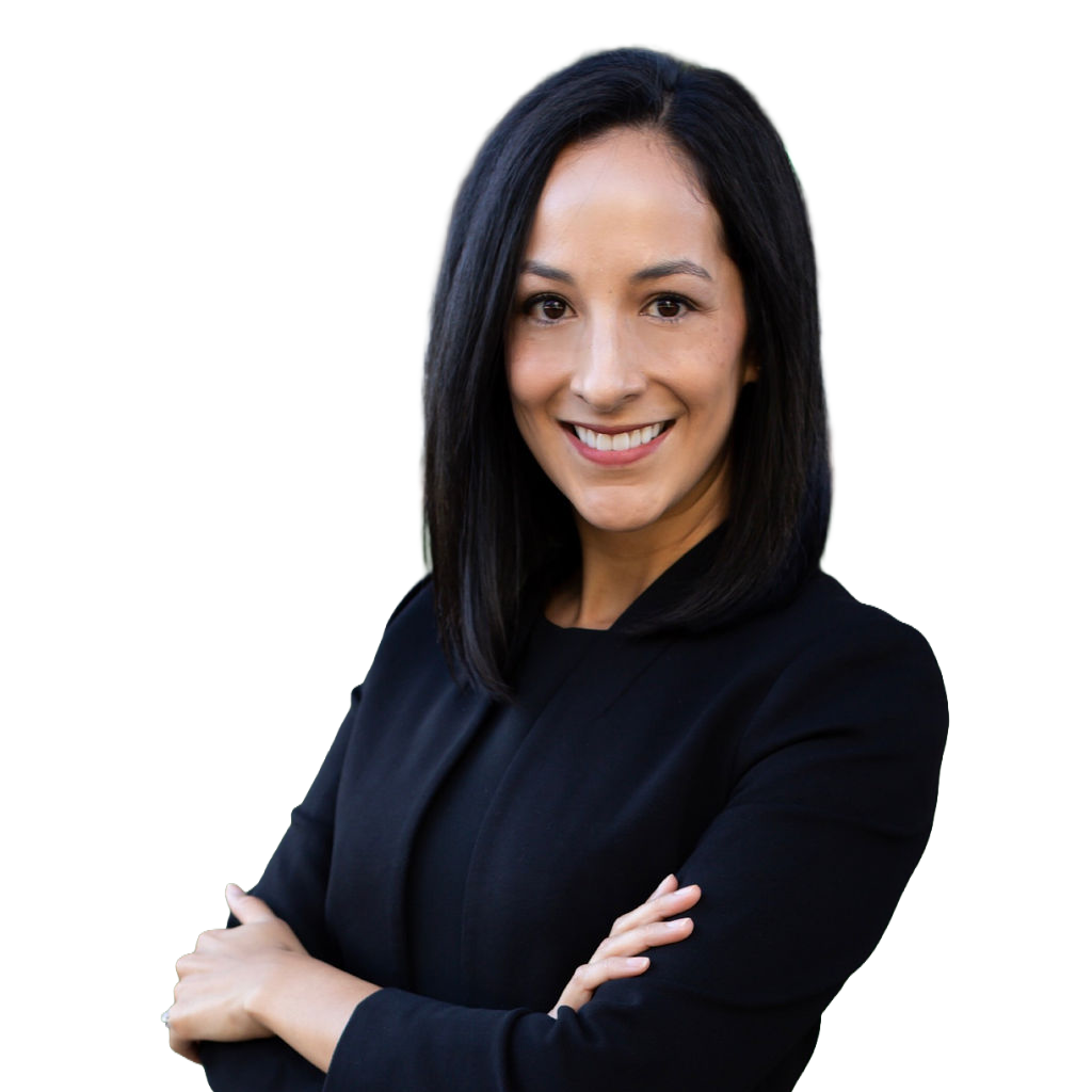 A professional woman with shoulder-length black hair, wearing a black blazer, smiling with arms crossed against a blurred outdoor background.