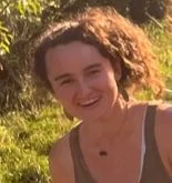 A woman with curly hair smiling outdoors in natural sunlight