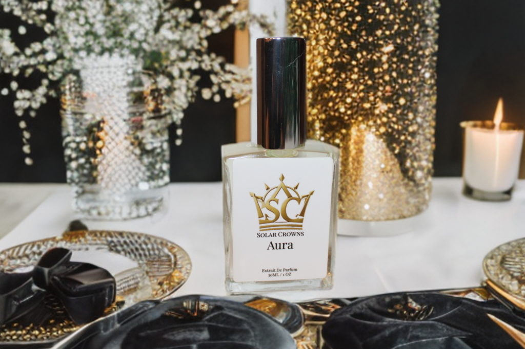 A perfume bottle labeled 'Solar Crowns Aura' on a white table, surrounded by decorative items including a gold tray, golden and silver vases, and a lit candle in the background.