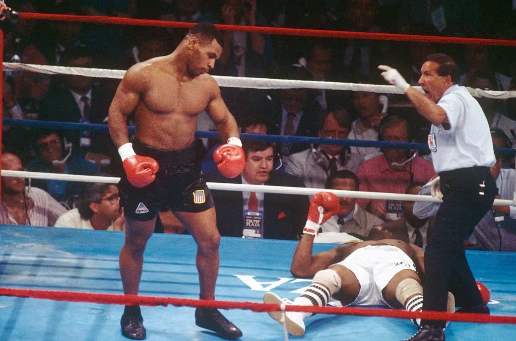 Tyson walks to a neutral corner as referee counts over a knocked down Michael Spinks