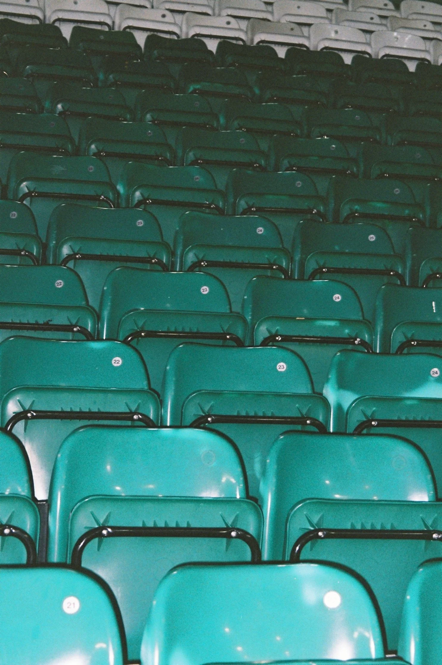 Stacked teal stadium seats with white number stickers, with some white seats in the background.