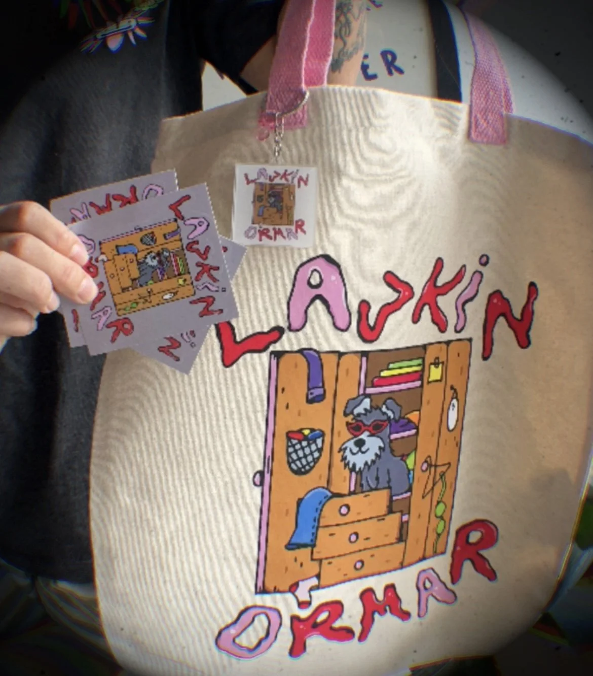 Person wearing an apron with the words 'LASKIN ORMAR' and a cartoon dog illustration, holding stickers featuring the same design.