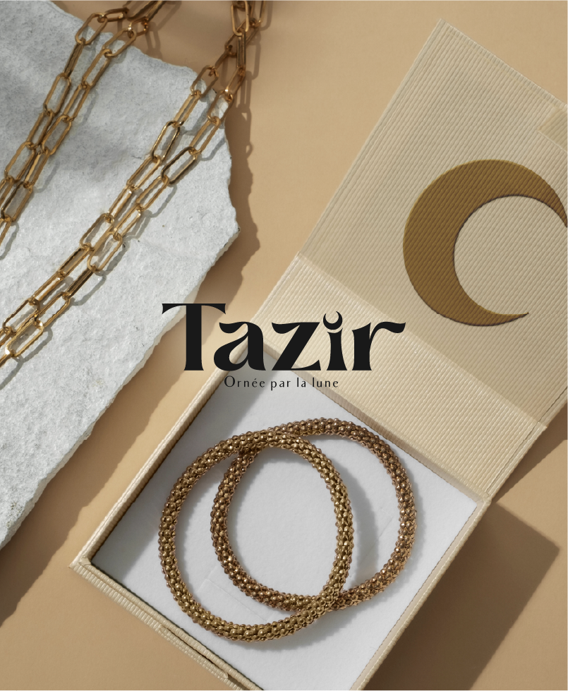 Deux bracelets en or dans une boîte, un collier en or posé sur une surface en pierre, et une carte avec un croissant de lune en or.