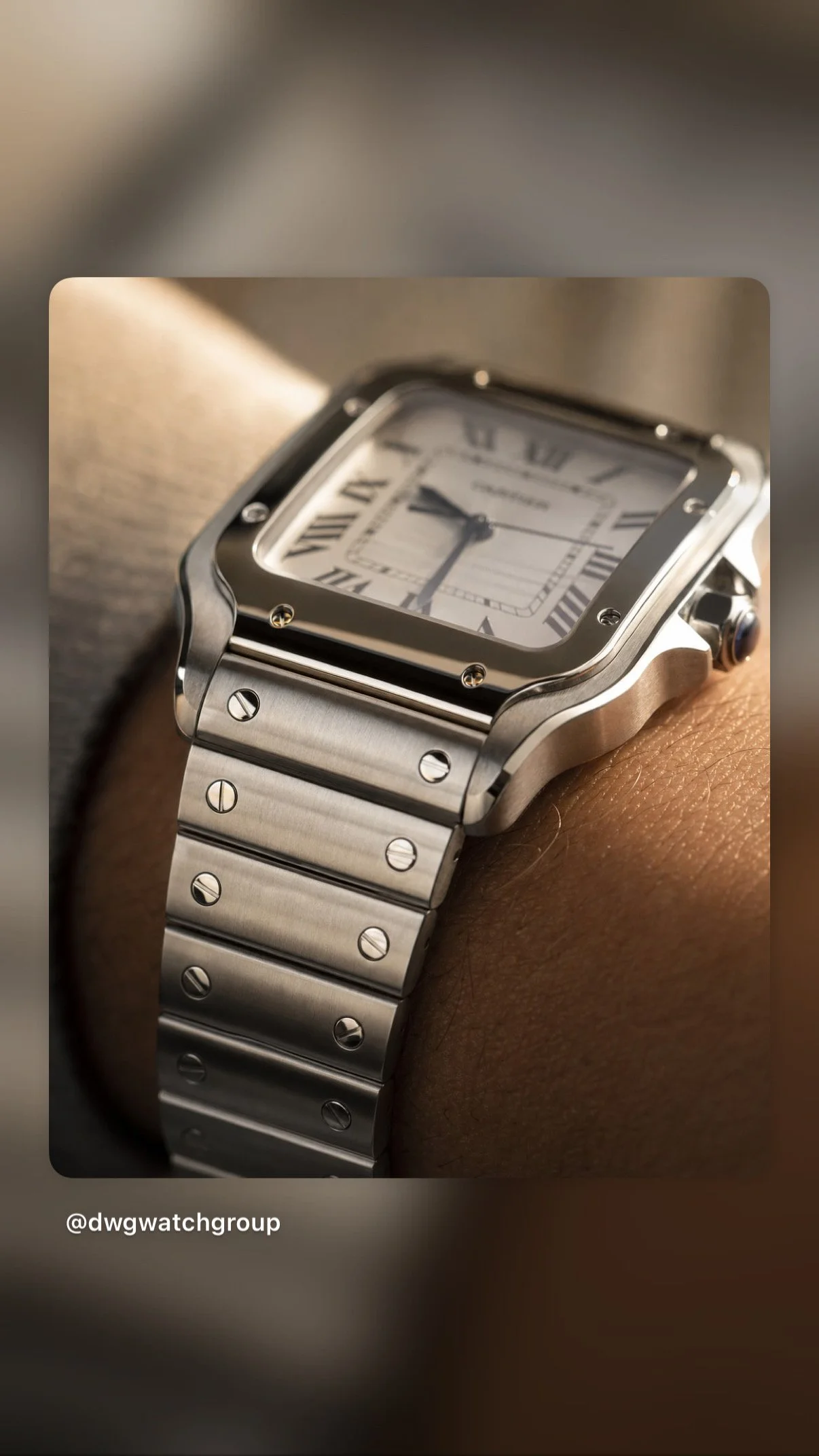 Close-up of a wristwatch with a square face, Roman numeral hour markers, and a metal bracelet, worn on a person's wrist.