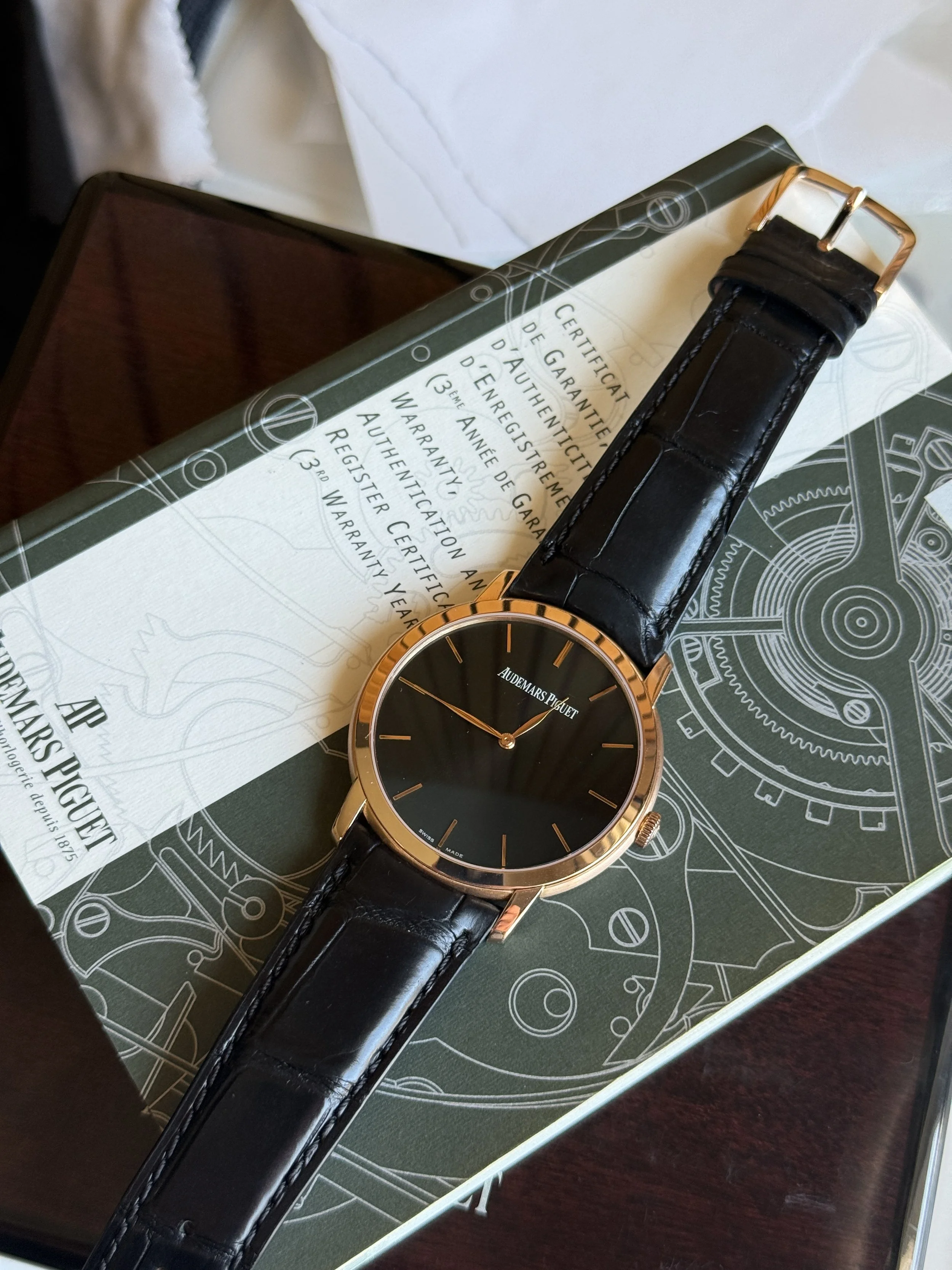 A luxury wristwatch with a black face and gold case is placed on a box and an official document with text in French.