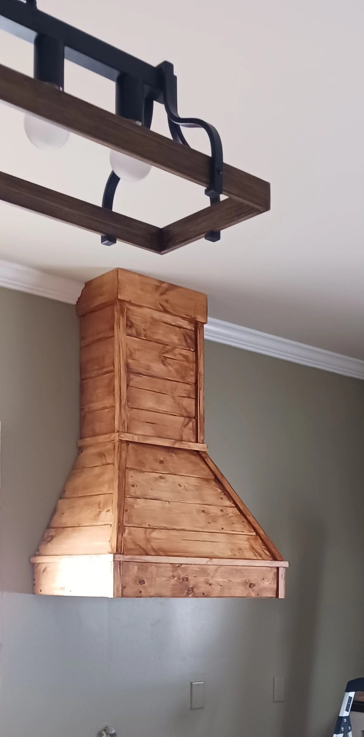 A wooden kitchen range hood mounted on a beige wall in a home interior.