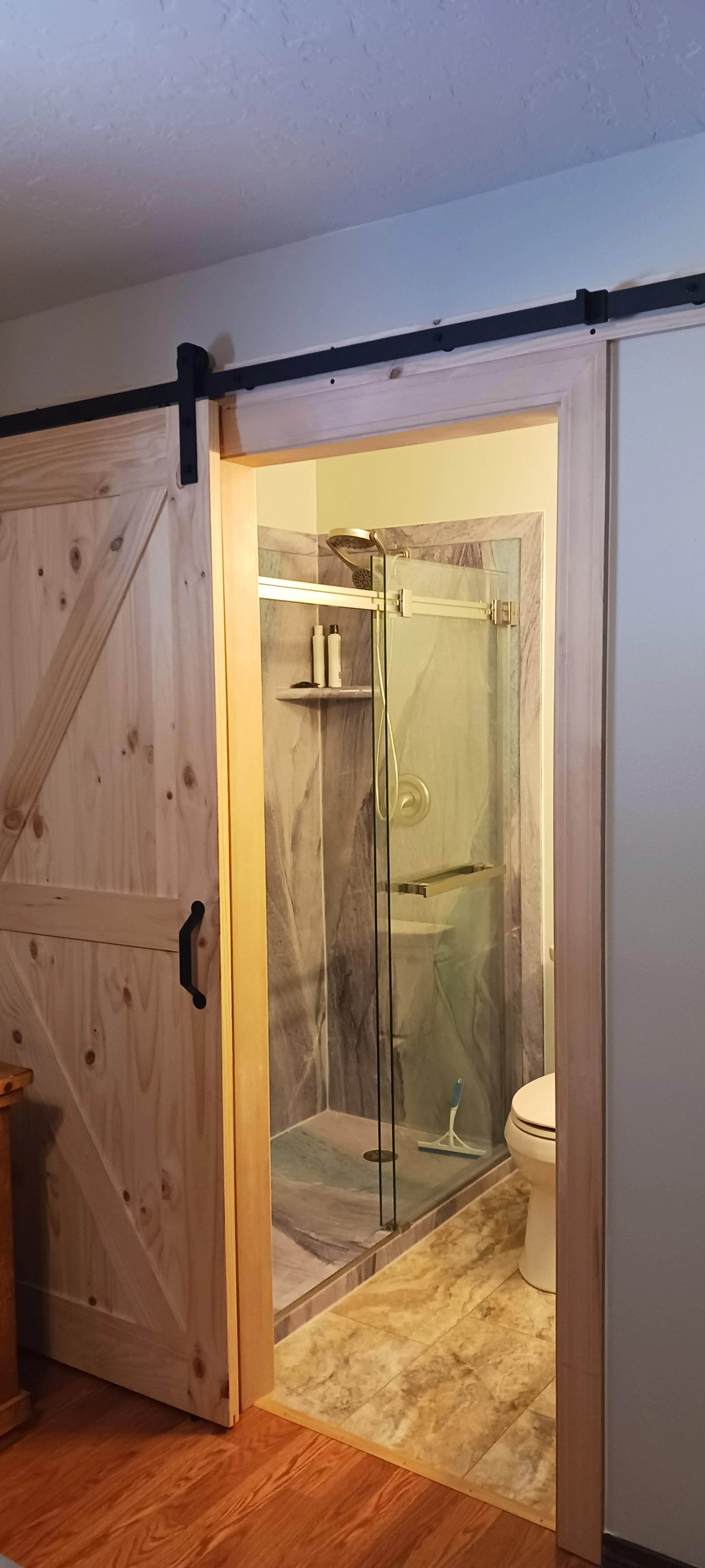 Bathroom with a glass shower enclosure, marble walls, and a toilet visible from the adjacent room.
