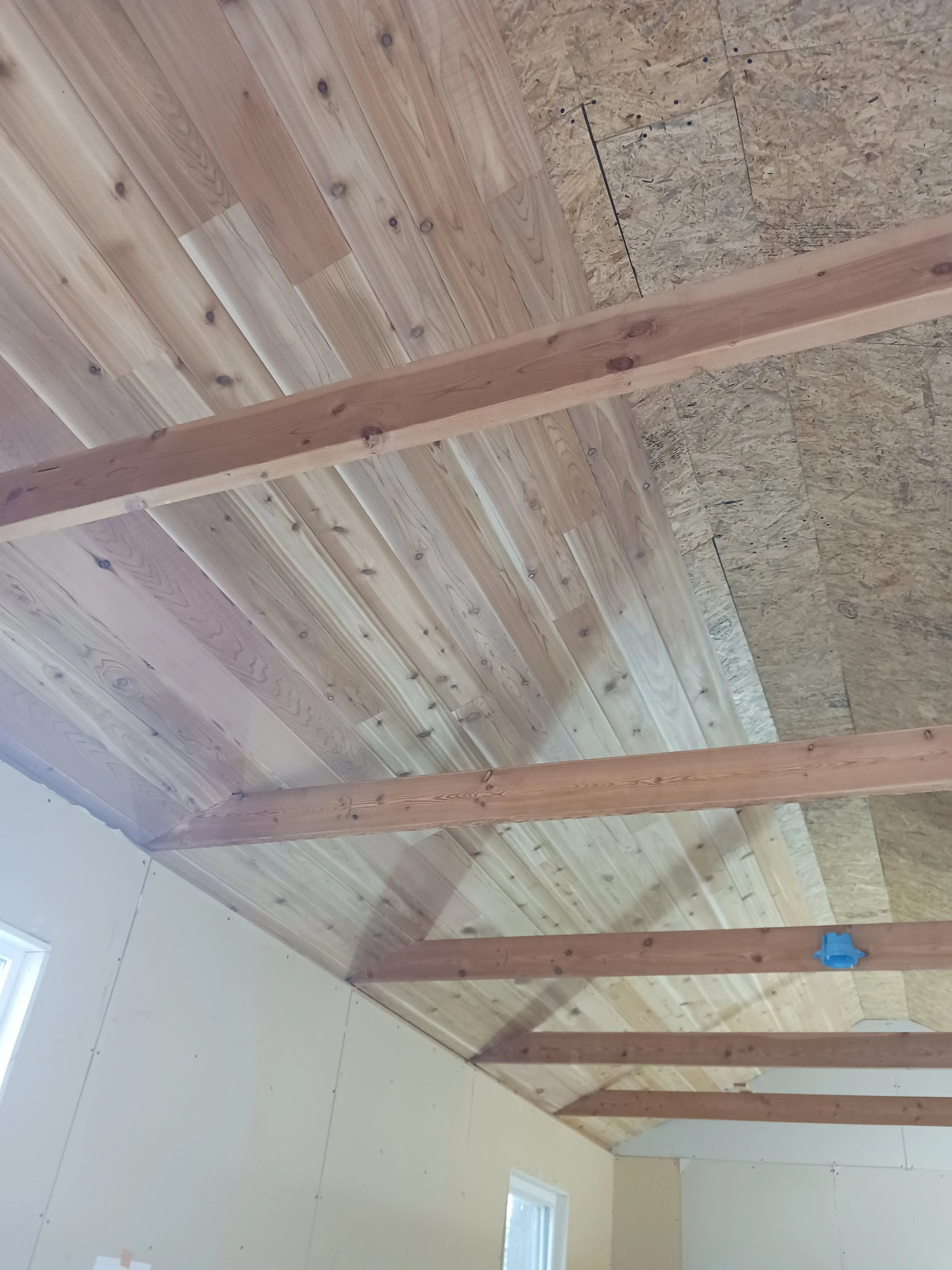 Photo of a room under construction with exposed wooden beams and partially finished wood-paneled ceiling.