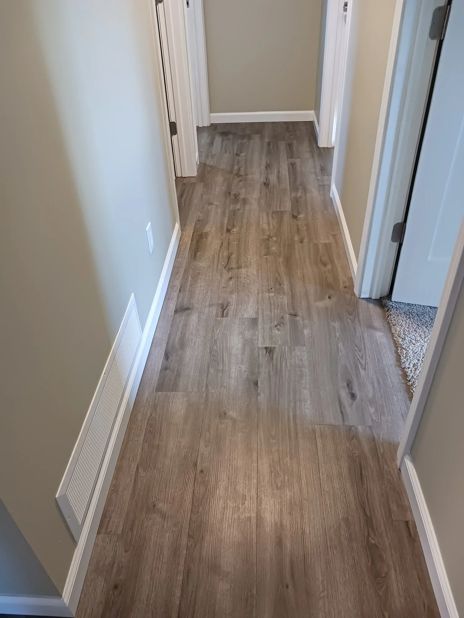 Hallway with wood flooring, beige walls, white baseboards, and open doors at the end.