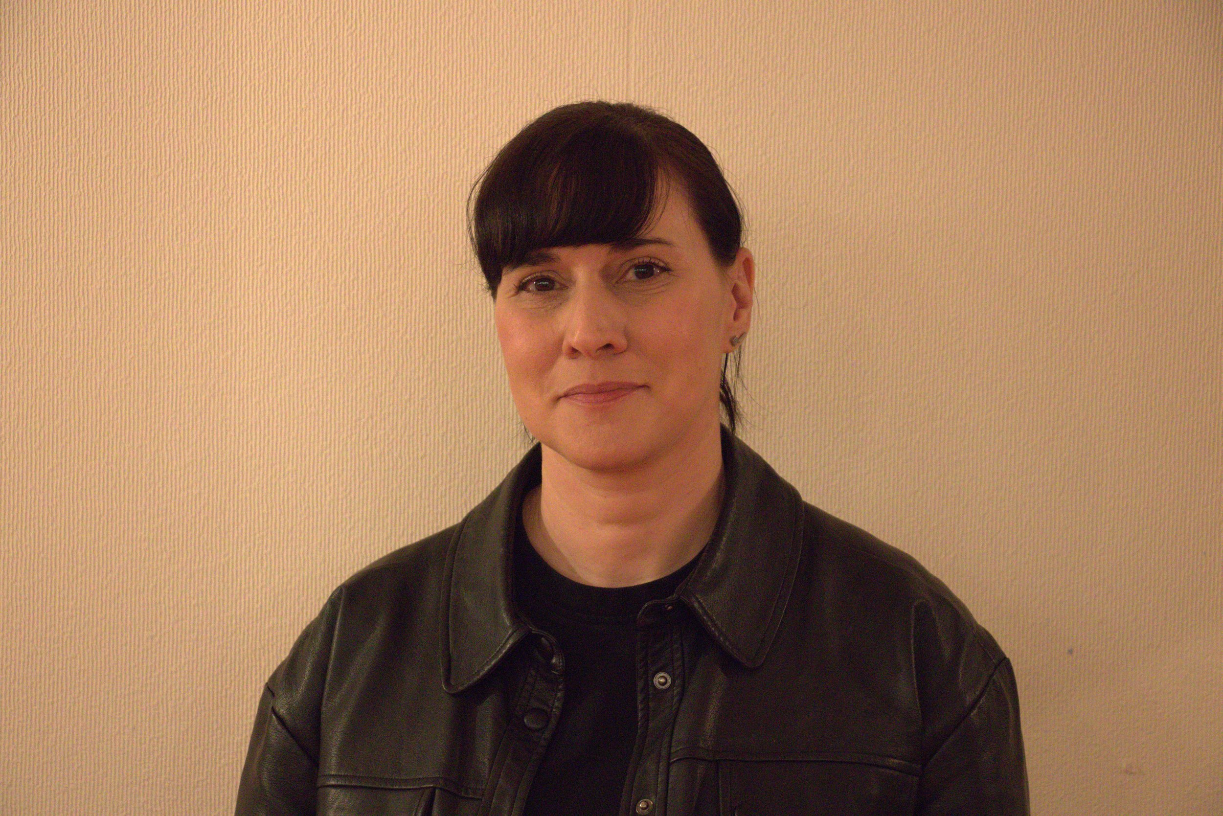 Portrait d'une femme portant une veste en cuir noire, avec un fond beige