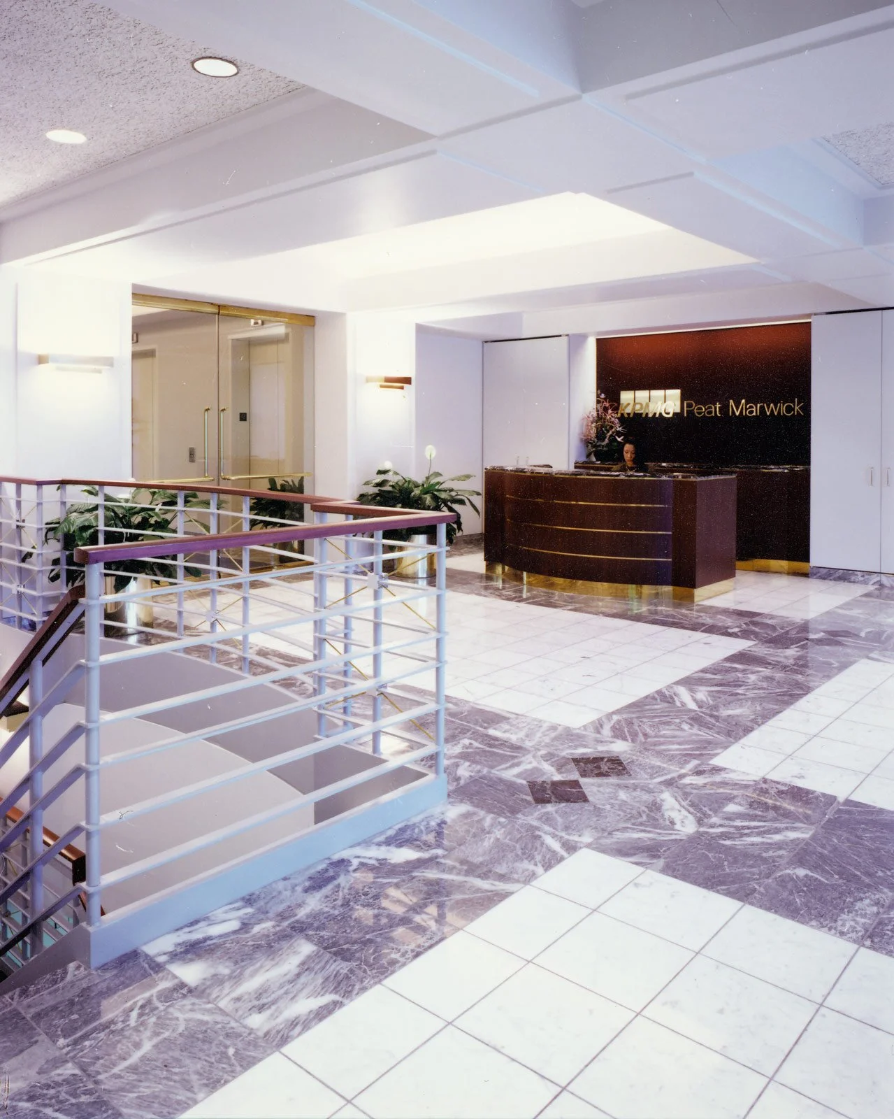 Lobby area with a reception desk, plants, marble tile floors, and elevator doors.