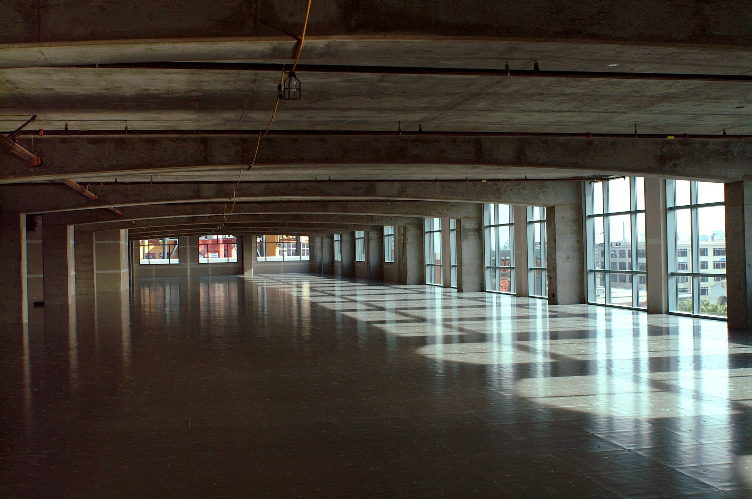 An unfinished high-rise building interior with large windows, concrete ceilings and floors, and exposed piping.