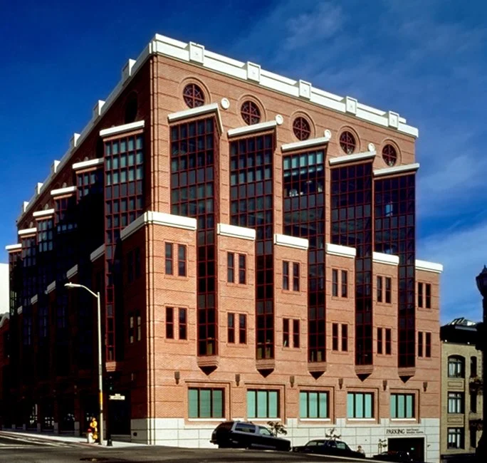 A large red brick building with multiple large windows and a modern architectural style, set against a blue sky.