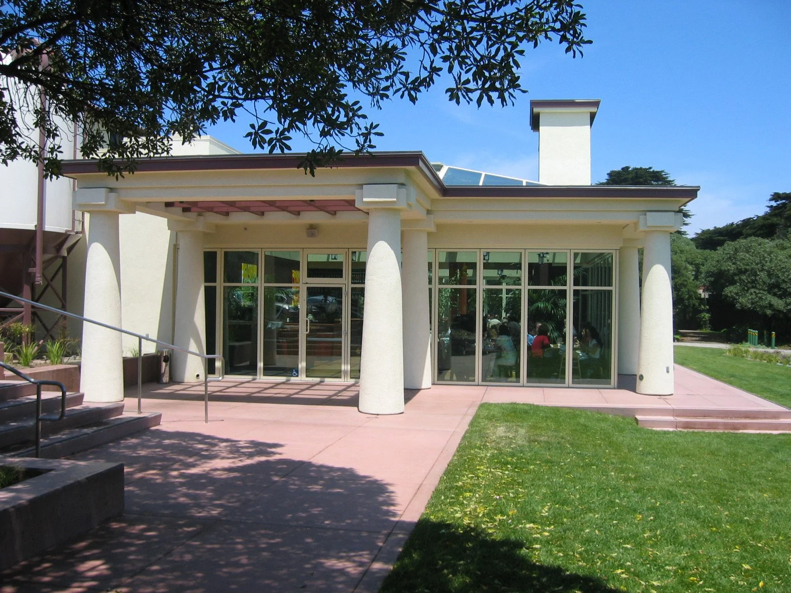 Modern building with large glass windows, surrounded by green lawn, trees, and clear blue sky.