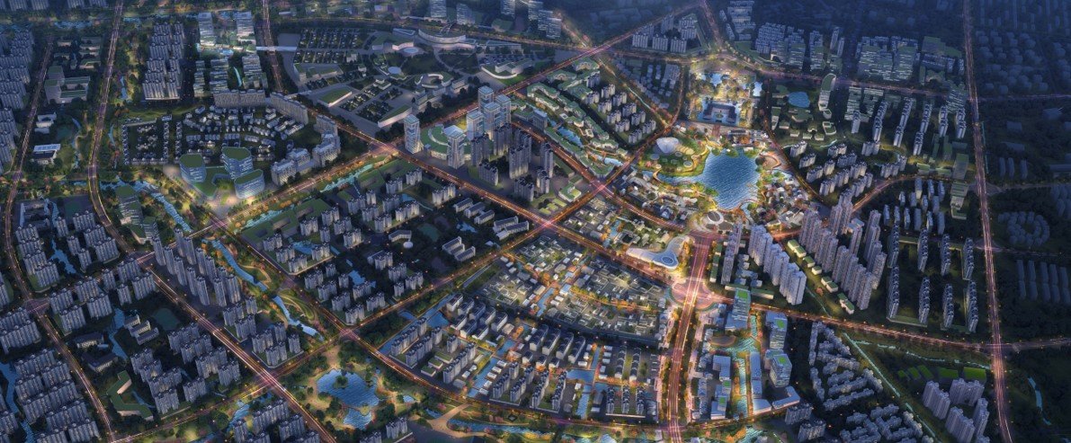 Nighttime aerial view of an illuminated urban city with high-rise buildings, roads, and a central park with a pond.