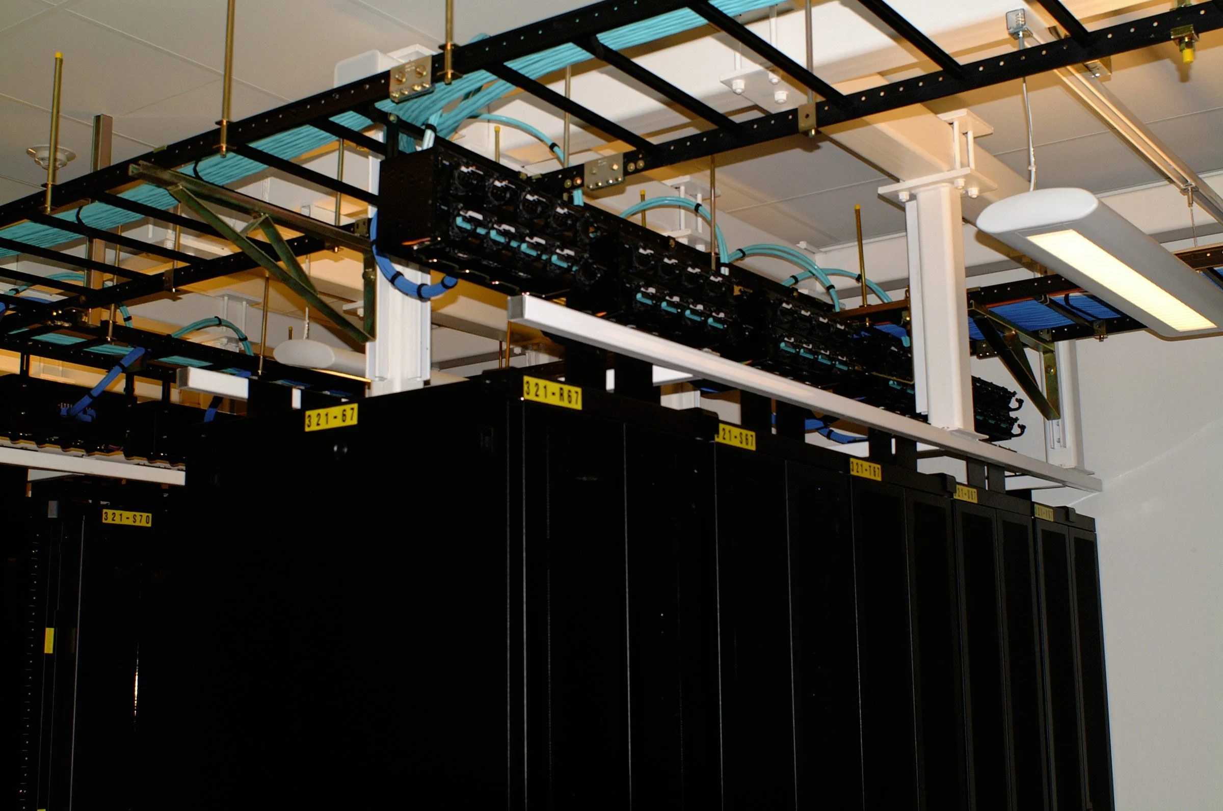 A server rack with multiple black server units, mounted on a white frame with white support beams, and various cabling and infrastructure components.