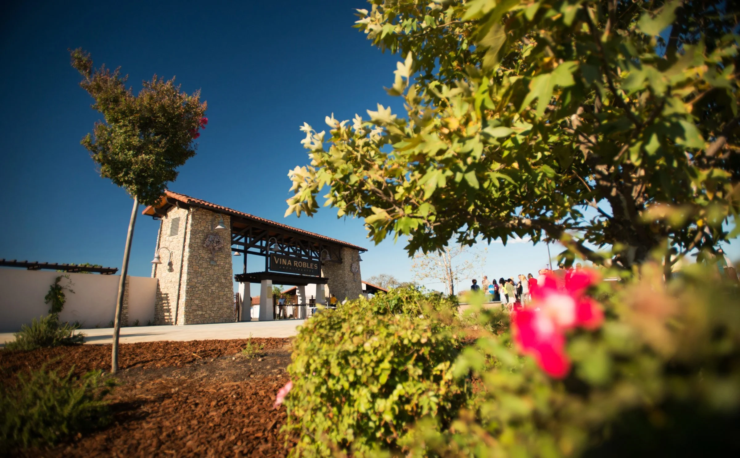 Entrance to Vina Robles winery with stone archway, green plants, and people gathering outside on a sunny day.