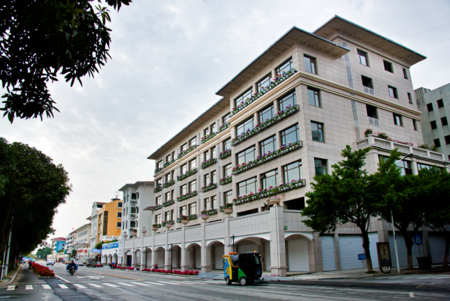 Multi-story beige building with balconies decorated with flowers on a city street