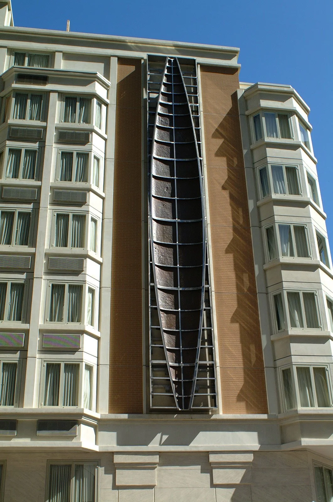 The exterior of a hotel under renovation, showing a large vertical slide or chute attached to the building, with scaffolding inside.