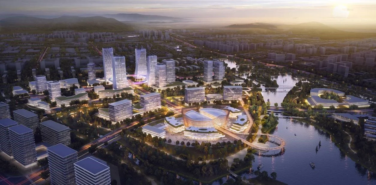 Aerial view of a modern cityscape at sunset with illuminated buildings, water bodies, and green spaces in a planned urban development.