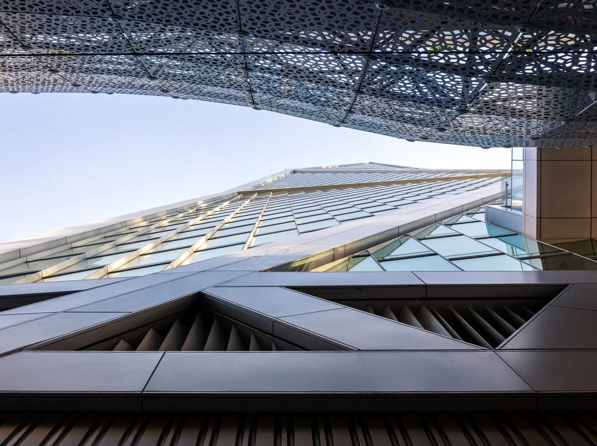 View looking up at modern skyscrapers with glass facades and intricate architectural details in a city.