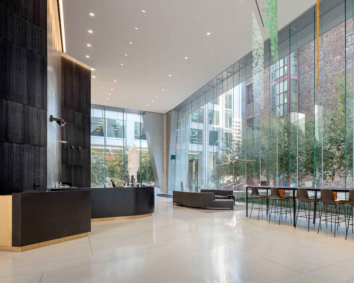 Modern hotel lobby with a reception desk, large glass windows, and seating area with barstools.