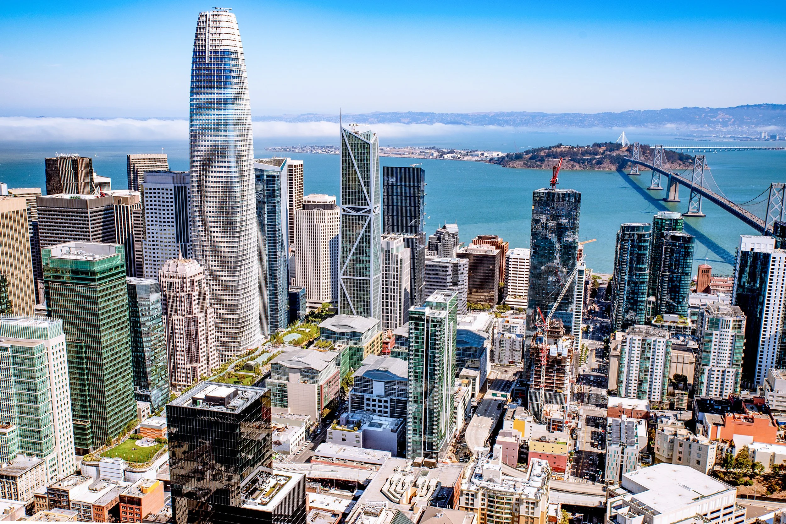 Aerial view of San Francisco skyline with tall skyscrapers, including the Salesforce Tower, and the San Francisco Bay in the background.